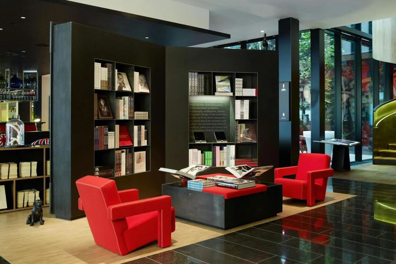 a library with two red chairs and books at citizenM London Bankside in London